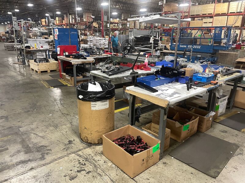 Bluegrass Living assembly area before - cluttered workbenches, parts in cardboard boxes on floor, no organization